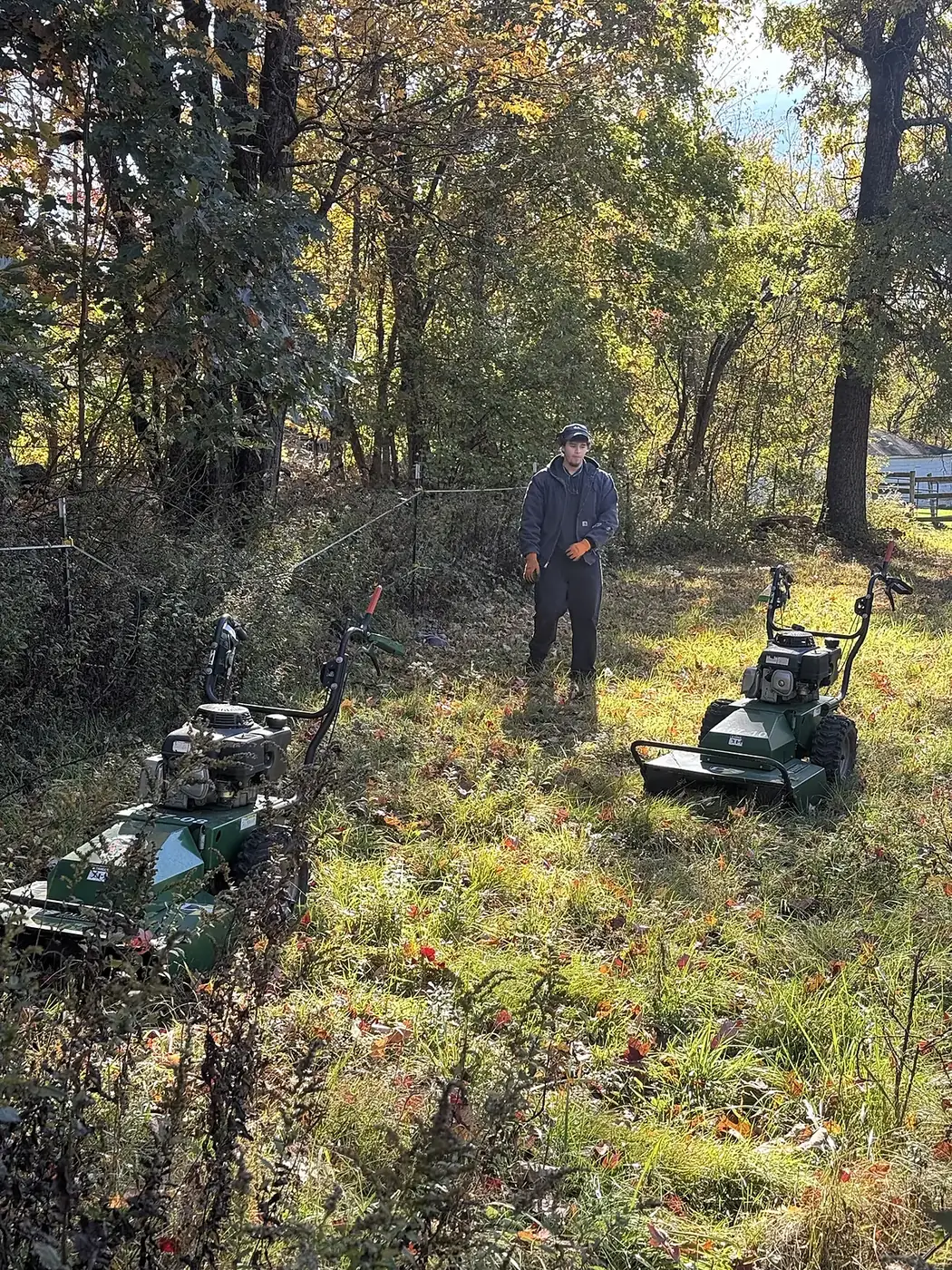 Crew member walking a freshly cleared path between two brush mowers