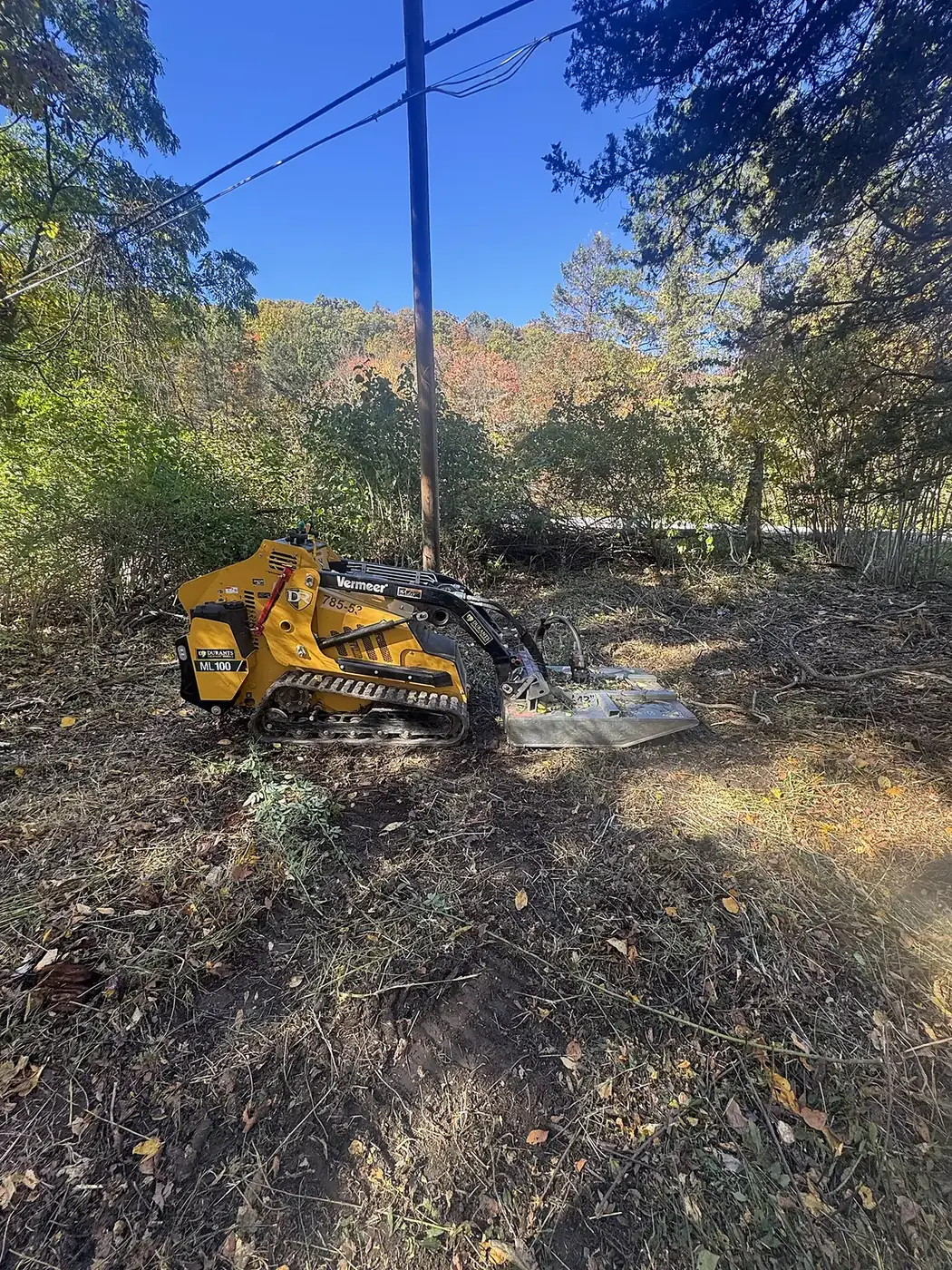 Tracked brush cutter on a cleared roadside lot under a blue sky