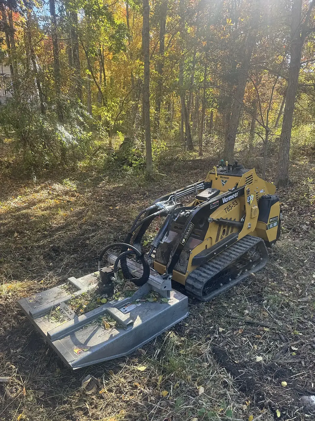 Tracked machine with a brush cutter parked on freshly cleared ground in the woods